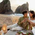 Coastal,Clinks.,Young,Romantic,Couple,Having,Picnic,On,Sandy,Beach